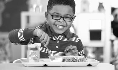 小学年龄的黑人男孩微笑着吃学校午餐