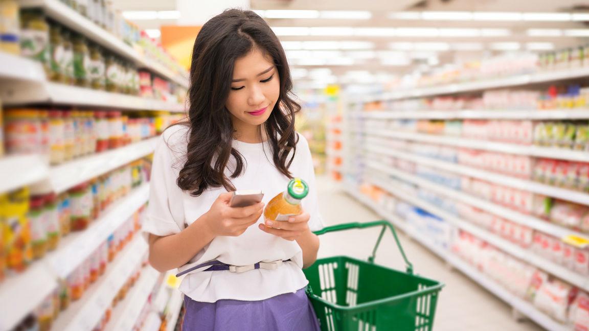 Asian Woman looking up ingredients on label using mobile phone