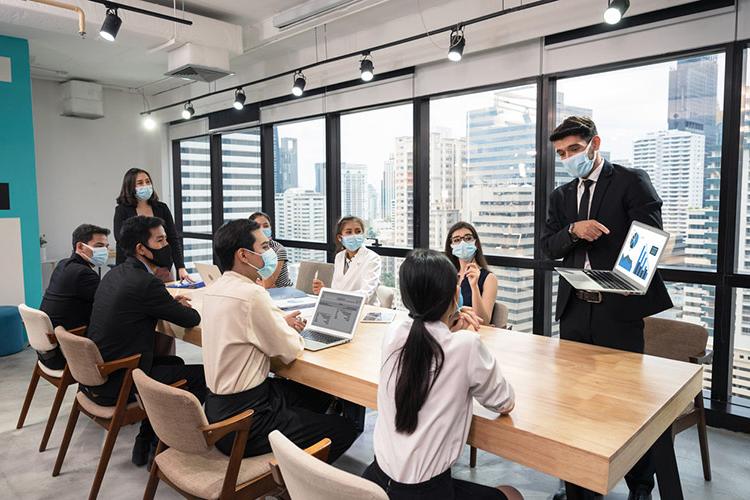 商人戴着口罩，在笔记本电脑上展示商业计划, 在病毒大流行的情况下，在现代办公室举行公司商务会议